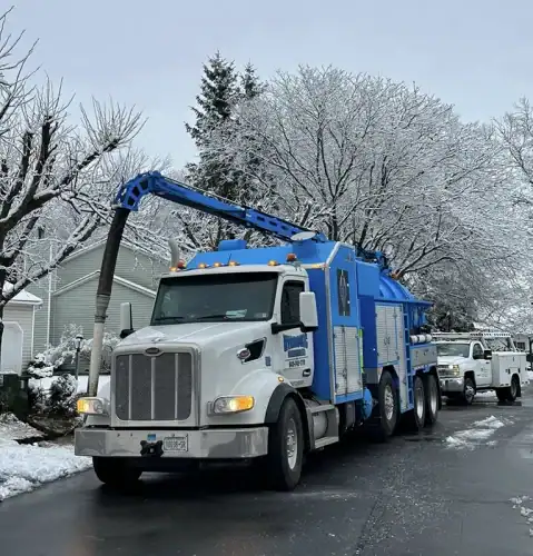 A blue and white Hydrovac Excavating truck is parked on a snowy street.