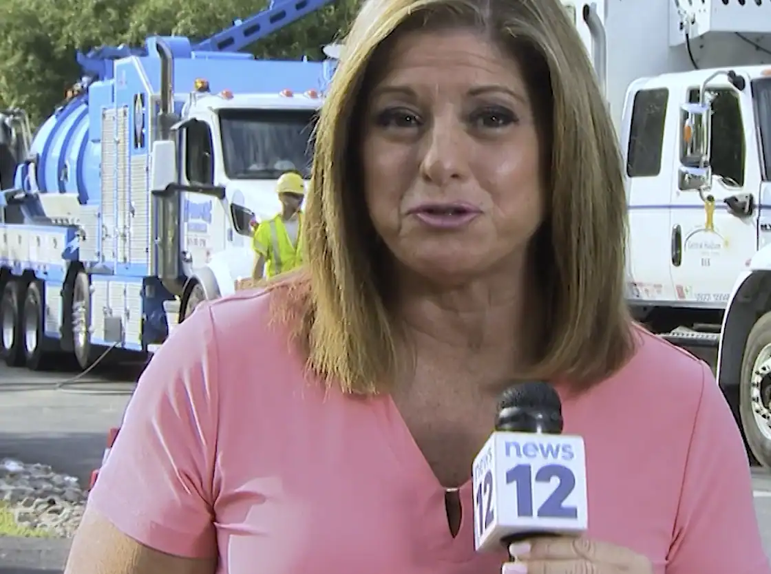 Newscaster in front hydrovac excavating trucks.